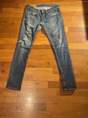 Blå slitna skinny jeans med hål - Säljer ett par blå Dondup jeans med slitningar och hål på framsidan av benen. Jeansen är i George modell och strl 31. Dem är 93cm långa och 38 cm bredda. Priset ej hugget.