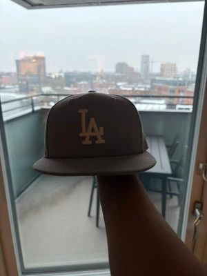 Grå LA Dodgers keps från New Era - Snygg grå keps från New Era med LA Dodgers-logga broderad framtill i vitt. Klassisk flat brim och broderad MLB-logga baktill. Perfekt för dig som vill ha en stilren och sportig look. Tillverkad i bomullstyg.