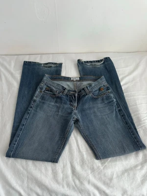 Lågmidjade jeans - Säljer ett par lågmidjade blå jeans från Tom Tailor med raka ben och slitna detaljer vid bensluten men går att klippas. Jeansen har fem fickor, knappgylf och är gjorda i mjuk denim med snygg tvätt. 