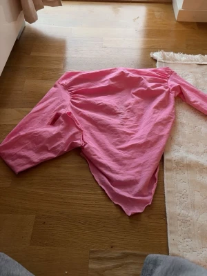 Rosa puffärm blus - Säljer en rosa blus med puffärmar och rund hals. Blusen har en lös passform och är tillverkad i ett mjukt, tunt tyg som känns bekvämt mot huden. Perfekt för dig som gillar färgglada och trendiga plagg.