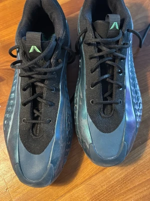 Ae 1s - Säljer ett par snygga Ae  från adidas i svart med blå metallicdetaljer och cool struktur på sidorna. Skorna har svart mesh upptill för bra ventilation och klassisk snörning. Perfekta för dig som vill ha stilrena och explosiva skor till träningen.