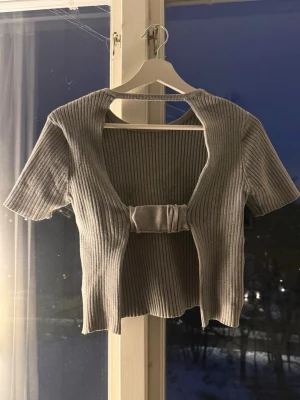 Grå ribbad croppad topp  - Trendig grå croppad topp i ribbad bomullsmix med korta ärmar och öppen framsida.