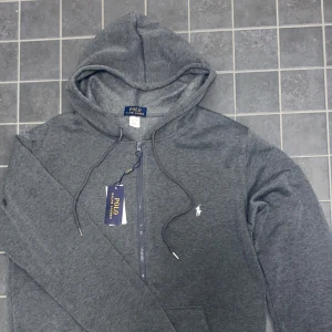 Grå hoodie från Polo Ralph Lauren - Pris kan diskuteras. Grå snygg ralph lauren zip. Provat den men aldrig använd bortsett från det. Den är jätte snygg och har ett jätteskönt material.  Lappen sitter även kvar på.
