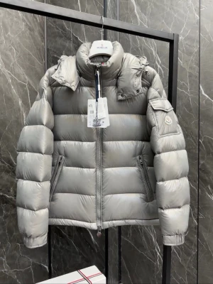  Moncler jacka  - Snygg silvergrå dunjacka från Moncler med hög krage, avtagbar huva och två dragkedjeförsedda fickor framtill. Jackan har Moncler-logga på ärmen och quiltad design som ger en puffig look. Perfekt för kalla vinterdagar.