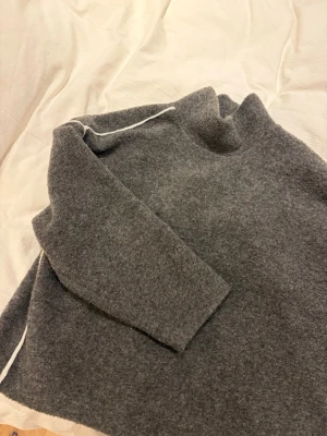 Grå stickad polotröja - Storlek M men passar även L. Mysig grå stickad polotröja från Zara med lös passform och långa ärmar.  Tröjan har en hög krage och diskreta vita sömdetaljer längs axlarna. Perfekt för kalla dagar och enkel att matcha med olika outfits.