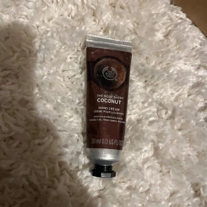 The Body Shop Coconut handkräm - Kokosdoftande handkräm från The Body Shop i en smidig tub på 30 ml. Tuben är brun med vita detaljer och har en metallisk skruvkork. Innehåller kokosolja som ger återfuktande effekt och en fräsch doft.