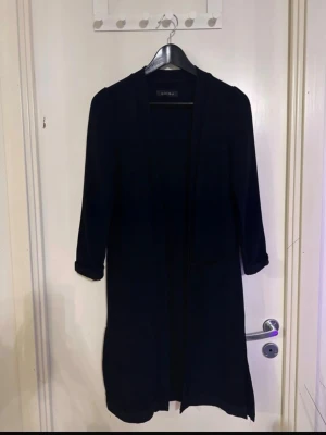 Svart lång cardigan från Carin Wester - Stilren svart lång cardigan från new yorker med öppen front och trekvartsärmar. Enkel design utan knappar eller fickor, perfekt att slänga över en t-shirt eller topp. Mjuk och följsam kvalitet som ger en avslappnad look.