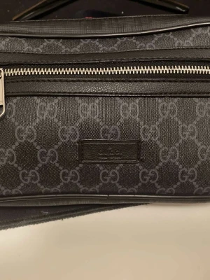 Svart GG Supreme handväska från Gucci - Snygg svart handväska från Gucci i GG Supreme-mönster. Väskan har silverfärgad dragkedja och detaljer i läder. Klassisk rektangulär form och diskret logotyp framtill. Perfekt för dig som gillar exklusiva accessoarer med ikonisk design.