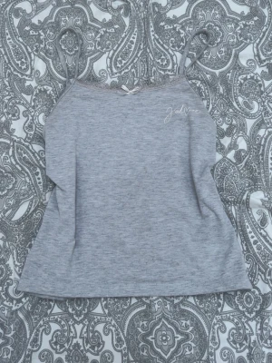 Grått linne med spets och rosett - Mysigt grått loungewear-linne med tunna axelband, spetskant upptill och liten söt rosett i mitten. Tryck med texten 'J'adore' på bröstet. Supergulligt och mysigt linne från Gina Tricot. Säljer därför att linner är för litet för mig, det har en liten fläck som man ser på sista bilden men ingenting man tänker på, går säkert bort i tvätt.