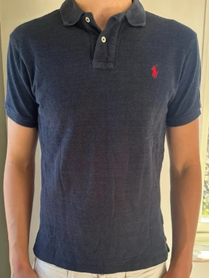 Ralph Lauren Navy Piké - Slim fit - Storlek S - Premium Polo Ralph Lauren piké i mjuk bomull med fantastisk komfort. Slim fit ger en modern siluett. Toppskick utan defekter! En lyxig och tidlös piké. 👕 Märke & Modell: Polo Ralph Lauren – Slim Fit 📏 Storlek & Passform: S/M (kolla måtten nedan!) – Slim fit 🧵 Material: 100% mjuk bomull 📐 Mått: Bröst: 50 cm Längd: 63 cm ✅ Skick: 9,5/10 - Nyskick, inga defekter ✨ Detaljer: Röd broderad logga, klassisk krage, mjuk yta 💰 Nypris: Ca 1300 kr ‼️ Skickas inom 24h ‼️ 