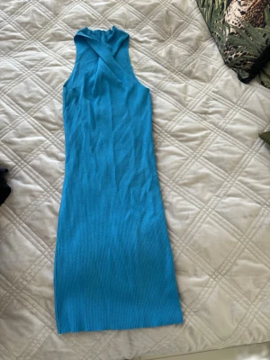 Blå ribbad ärmlös klänning - Säljer en blå ribbad klänning med hög hals och ärmlös design. Klänningen har en kroppsnära passform och är gjord i ett stretchigt material som känns bekvämt. Perfekt för dig som gillar en enkel men snygg stil.