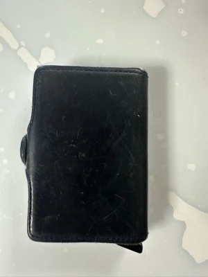 Mörkblå plånbok från Secrid  - Dubbelfack plånbok i läder  från Secrid med smart metallfack för kort. Plånboken har en stilren, rektangulär form och stängs med tryckknapp. Perfekt för dig som vill ha både klassisk look och modern funktion. Repor förekommer 