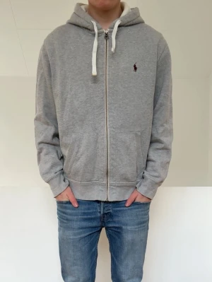 Grå Ralph Lauren zip hoodie - Säljer en fet raffe hoodie i färgen grå. Hoodien är k bra skivk utan nåra defekter och är strl L men sitter som en M. Hör gärna av er vid frågor elr funderingar!!