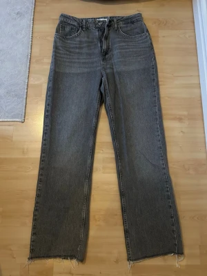 Grå raka jeans med rå kant - Original storlek 38 men passar även 36 (lite liten i storlek) Säljer ett par grå jeans med rak passform och hög midja. Jeansen har råa, fransiga benslut och klassisk femficksdesign. Tillverkade i denim med en vintagekänsla, perfekta för en avslappnad och trendig look.