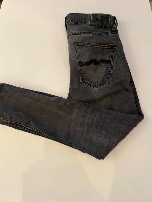 Svarta slim fit jeans från Nudie Jeans - Storlek: 30/32.                                                  Snygga svarta slim fit jeans från Nudie Jeans med klassisk femficksdesign och diskret logga på bakfickan. Jeansen har en tvättad look och smal passform som ger en modern stil. Tillverkade i mjukt denimtyg för skön känsla.                                      Skick: 5/10                                                                            Defekter: trasig ficka (kan sys ihop)