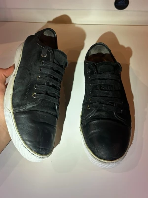 Svarta lanvins - Svarta mockaskor med blank cap toe från Lanvin, modell DBB1, storlek UK 8 (ungefär EU 42–43). Skorna är i bra skick, med två mindre defekter: vissa sömmar har gått upp och det finns ett hål i sulan, men en formad plastpåse fungerar som skydd, så de är fortfarande fullt användbara. Nypris ligger på 4499 kr. Inga originaltillbehör medföljer.  Kolla gärna in profilen också, där finns flera märkeskläder och skor – du hittar säkert något mer som passar 😉💯 Hör av dig om du undrar något!
