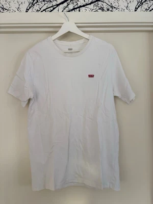 Vit t-shirt från Levi's med logga - Klassisk vit t-shirt från Levi's med liten röd logga på bröstet. T-shirten har rund halsringning. Ny pris 200kr mitt pris 100kr