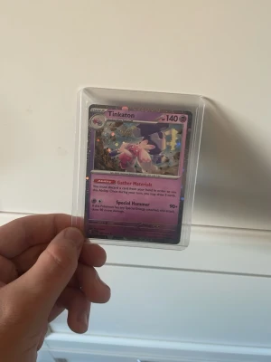 Pokémonkort Tinkaton Holo - Säljer ett Pokémonkort med Tinkaton, holografisk design och lila bakgrund. Kortet har 140 HP och visar Tinkaton med sin stora hammare. Kortet är inplastat i ett skyddsfodral och har coola effekter och detaljer.