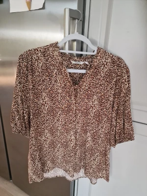 Brunmönstrad blus med v-ringning - Säljer en snygg blus med brunt och vitt leopardmönster. Materialet känns mjukt och följsamt, perfekt för en trendig look. Passar till både jeans och kjol.
