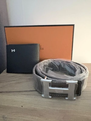 Svart bälte med silver H-spänne - Snyggt svart bälte från  med ett stort H-format spänne i silverfärg. Bältet är gjort i skinn och har en klassisk, stilren design som passar till många olika outfits. Perfekt accessoar för dig som gillar exklusiva detaljer.