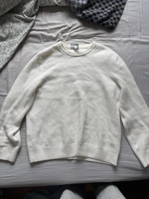 Vit stickad tröja från H&M - Säljer en stilren vit stickad tröja från H&M. Tröjan har rund halsringning, diskret strukturstickning och ribbade muddar vid ärmslut och nederkant. Perfekt för lager på lager och enkel att matcha med olika outfits.
