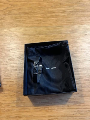 Saint Laurent Armband - Säljer nu detta stilrena autentiska armband ifrån Saint Laurent, skick 7/10. Magnetiskt. Den enda defekten är att insidan av armbandet är lite slitet och att texten där man knäpper armbandet är lite slitet men det är inget som syns när man har på sig det. Nypris ca 2700. Allt medkommer på bilden, storlek: 17cm 