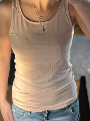 Ljusrosa linne - Säljer en enkel och stilren ljusrosa linnetopp i bomull. Toppen är ärmlös med rund halsringning och har en slim passform som sitter snyggt mot kroppen. Perfekt till jeans eller shorts för en avslappnad look. Storlek 158/164 från H&M så skulle säga att den passar en xs eller liten s💕