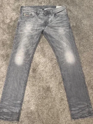 Diesel Jeans - Snygga gråa slim fit jeans från Diesel med slitningar och ljusa partier på knäna. Klassisk femficksmodell med detaljerad myntficka och patch bak i midjan. Jeansen har raka ben och är tillverkade i bomull för en bekväm känsla.