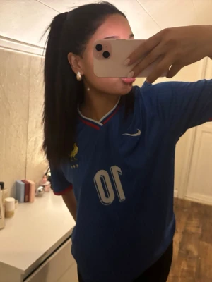 Blå Frankrike fotbollströja Nike - Säljer en blå fotbollströja från Nike med Frankrikes landslagsemblem och nummer 10 på bröstet. Tröjan har V-ringning med röd, vit och blå kant samt två stjärnor ovanför emblemet. Perfekt för dig som älskar fotboll och vill ha en klassisk supportertröja.