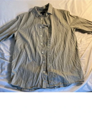 Grön skjorta från Gant i bomull - Klassisk grön skjorta från Gant med broderad logga på bröstet. Skjortan har lång ärm, knappar framtill och en avslappnad passform. Tillverkad i mjuk bomull som känns skön mot huden. Perfekt för en clean och stilren look. Passar dig som är runt 170cm lång.