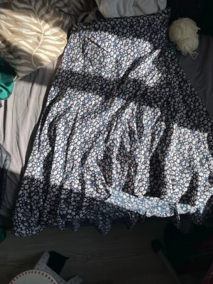 Blommig långkjol från Seaside - Supersöt långkjol från Seaside med mörkblå botten och vita blommor med röda detaljer. Kjolen har en flowy passform och är perfekt för dig som gillar en romantisk och avslappnad stil. Tillverkad i mjukt och lätt polyester som känns skönt mot huden.