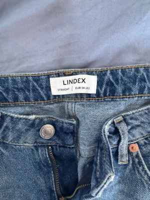 Blå raka jeans från Lindex - Säljer ett par klassiska blå raka jeans från Lindex i storlek EUR 34. Jeansen har hög midja, dragkedjegylf och knapp, samt fem fickor. Materialet är slitstark denim i 100% bomull. Perfekta till en avslappnad och trendig look. Sitter som Zaras wide jeans 