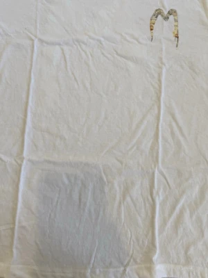 Vit t-shirt med grafiskt M-tryck - Snygg vit t-shirt med ett stort grafiskt M-tryck på bröstet i beige och grå toner. T-shirten har klassisk passform och rund hals. Perfekt för dig som gillar stilrena plagg med en twist.