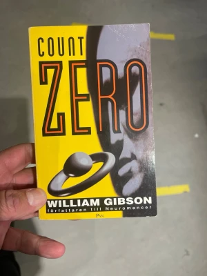 Count Zero av William Gibson - Count Zero av William Gibson är en pocketbok med gul och svart framsida. Omslaget har futuristisk design med stora bokstäver och en abstrakt illustration. Boken är på svenska och författaren är känd för Neuromancer.