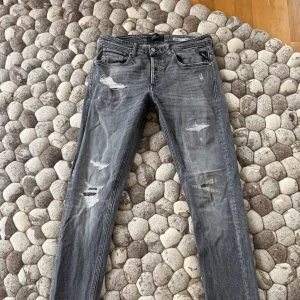 Grå  jeans från Replay - Säljer ett par grå jeans från Replay med slitningar och distressed detaljer. Modellen är smal och har klassisk femficksdesign. Mkt fint skick. Stl 30/34