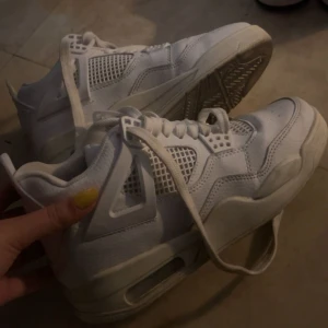Nike Air Jordan 4 helvita sneakers - Säljer ett par Nike Air Jordan 4 i helvitt skinn med meshpaneler och klassiska detaljer. Skorna har snörning, rund tå och en chunky sula med synlig Air-enhet. Perfekta för dig som gillar stilrena och ikoniska sneakers. Storlek 38/39