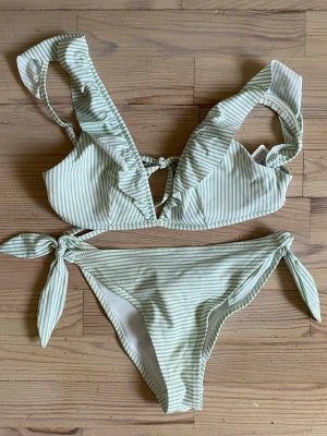 Grönvit randig bikini med volang - Jättesöt och unik bikini med volang från H&M. OBS: sista sista bilden visar en blå fläck på rumpan, men som göms av att tyget är skrynkligt. Jag erbjuder RABATT vid köp av flera plagg/varor 🌸✨