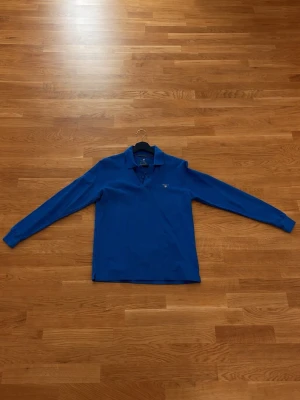 Blå långärmad pikétröja Gant - Klassisk blå långärmad pikétröja från Gant med krage och knappar framtill. Tillverkad i mjuk bomull som känns skön mot huden. Perfekt för dig som gillar en stilren och enkel look. | Pris kanske kan diskuteras🤝