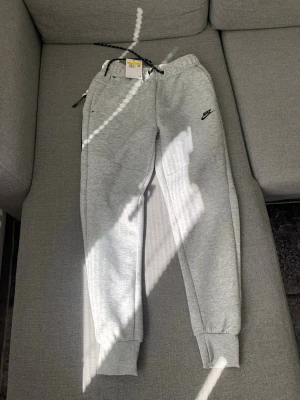 Grå mjukisbyxor från Nike(lägg bara ett bud så är den din) - Snygga grå mjukisbyxor från Nike med svart logga på vänster ben. Byxorna har dragsko i midjan, muddar vid bensluten och praktiska sidofickor. Perfekta för en avslappnad och sportig stil. Tillverkade i mjukt och bekvämt material. Pris kan diskuteras!!!