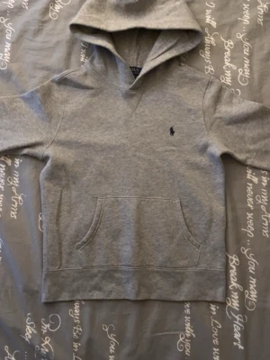 Grå hoodie från Polo Ralph Lauren - Snygg grå hoodie från Polo Ralph Lauren med klassisk huva och känguruficka. Diskret broderad logga på bröstet. Perfekt för en avslappnad och stilren look. Mjuk bomullsblandning som är skön att ha på sig hela dagen.