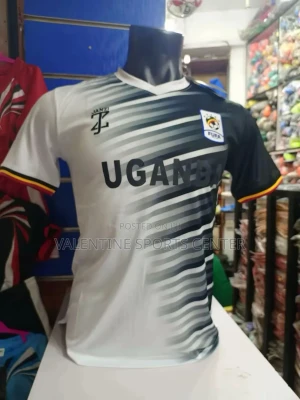 Uganda fotbollströja svart/vit - Snygg fotbollströja från Uganda-tryck och FUFA-logga. Tröjan är svart och vit med diagonala ränder och har färgdetaljer i rött, gult och svart vid ärmsluten. Perfekt för dig som vill visa stöd för Ugandas landslag.