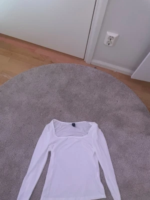 Vit långärmad topp med fyrkantig ringning - Säljer en stilren vit långärmad topp med fyrkantig ringning. Toppen har en slim passform och är perfekt att matcha med både jeans och kjol. Materialet känns mjukt och stretchigt, vilket gör den bekväm att bära hela dagen.