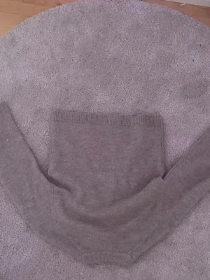 Grå stickad tröja med rund hals - Mysig grå stickad tröja med rund hals och ribbade muddar vid ärmslut och nederkant. Perfekt för lager-på-lager och enkel att matcha med jeans eller kjol. Klassisk och stilren design utan synliga loggor eller mönster.