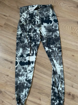 Tie-dye leggings i svart och beige - Säljer ett par trendiga leggings med tie-dye mönster i svart, beige och grå toner. De har en smal passform och elastisk midja för skön komfort. Perfekta för dig som vill sticka ut med en unik stil.