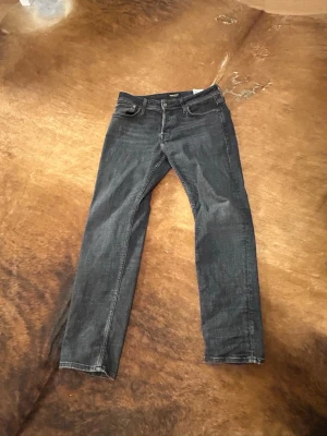Grå/svarta Jack&jones tapered/mike fit jeans - Säljer ett par grå svarta jeans med klassisk femficksdesign och raka ben. Jeansen har snygga kontrastsömmar och är tillverkade i denim. Perfekta för dig som gillar en enkel och stilren look.