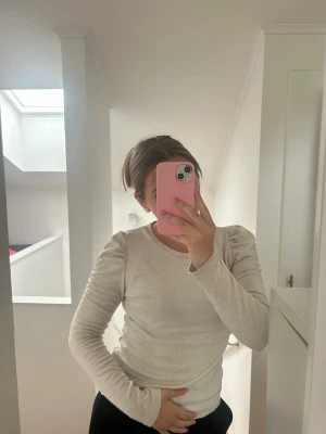 Ljusbeige långärmad topp - Säljer en ljusbeige långärmad topp med rund halsringning och figurnära passform. Toppen är enkel och stilren, perfekt att matcha med olika outfits. Materialet känns mjukt och stretchigt, troligtvis bomull eller polyester.