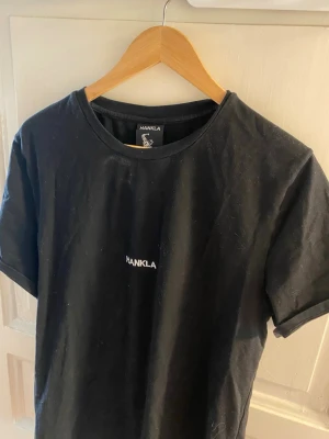 Svart t-shirt från Hankla - Svart t-shirt från Hankla med enkel och stilren design. T-shirten har rund halsringning och korta ärmar. Liten vit Hankla-logga broderad på bröstet. Perfekt för en avslappnad look.