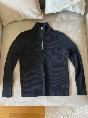 Svart stickad tröja med dragkedja - Snygg svart stickad tröja från Jack & Jones med hög krage och halv dragkedja framtill. Tröjan har ribbad struktur och långa ärmar, perfekt för kyligare dagar. Enkel och stilren design som passar till det mesta.