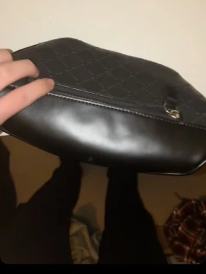 Svart axelväska från Gg - Snygg svart axelväska från Gg med klassiskt GG-mönster och detaljer i svart läder. Väskan har en justerbar rem, dragkedja upptill och en praktisk ytterficka med dragkedja. Perfekt för dig som vill ha en stilren och trendig accessoar.
