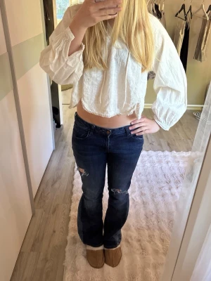 Mörkblå bootcut jeans med slitningar - Snygga mörkblå bootcut jeans med slitningar på knäna och klassisk femficksdesign. Jeansen har en låg midja och stängs med knapp och dragkedja. Perfekta för en avslappnad och trendig look. 😊😊